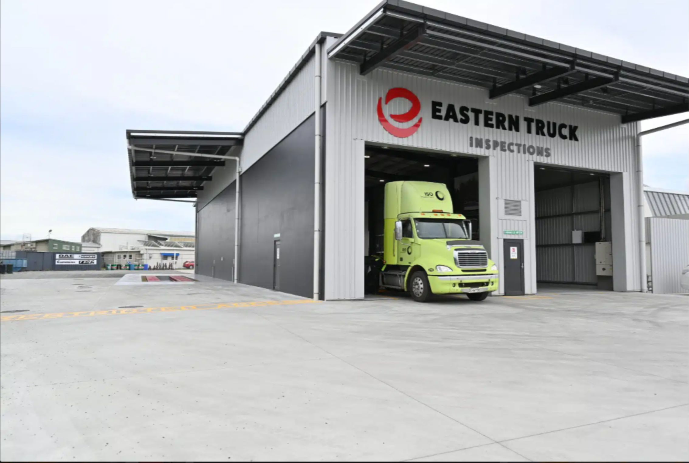 Large grey truck inspection building with green truck in open roller door