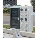 medium size switchboard with distribution and outlets mounted outdoors next to a wire fence at a refrigerated truck depot.