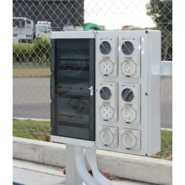 medium size switchboard with distribution and outlets mounted outdoors next to a wire fence at a refrigerated truck depot.